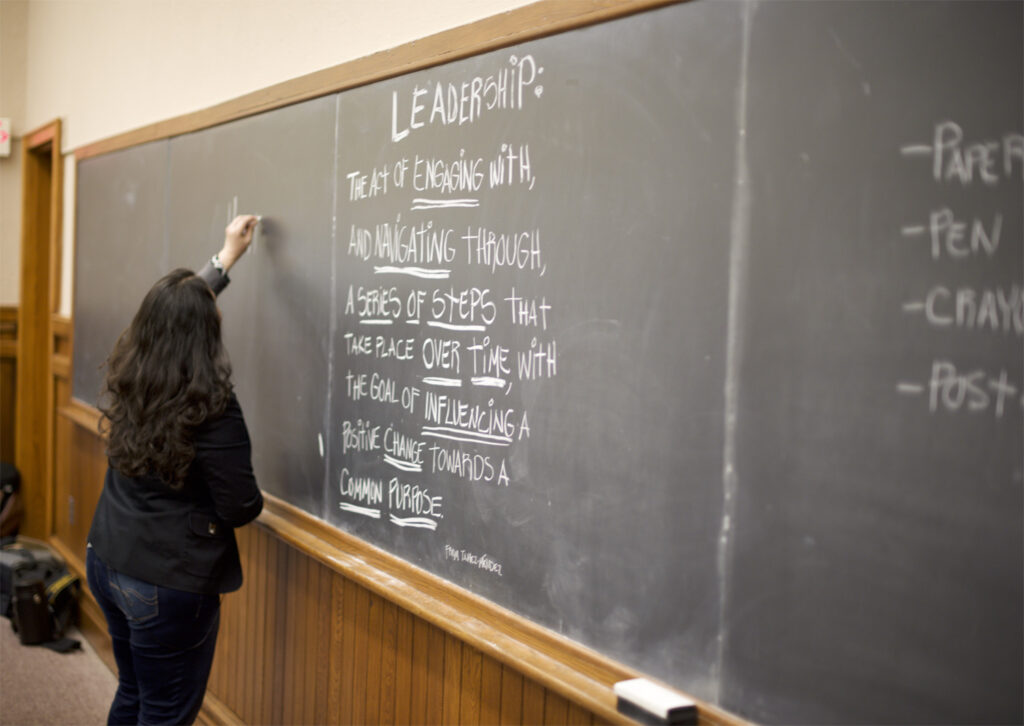 Woman writes leadership definition on chalkboard.